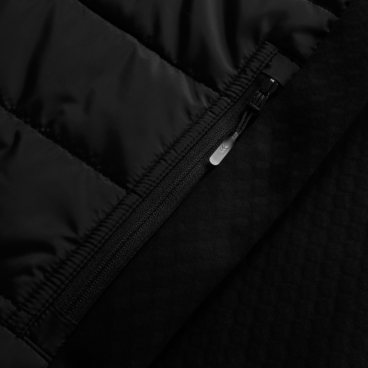 Close-up of a black zippered pocket on the Ireland 25/26 Elite Gilet by Canterbury, showcasing its quilted, textured fabric, detailed stitching, and shiny zipper pull.