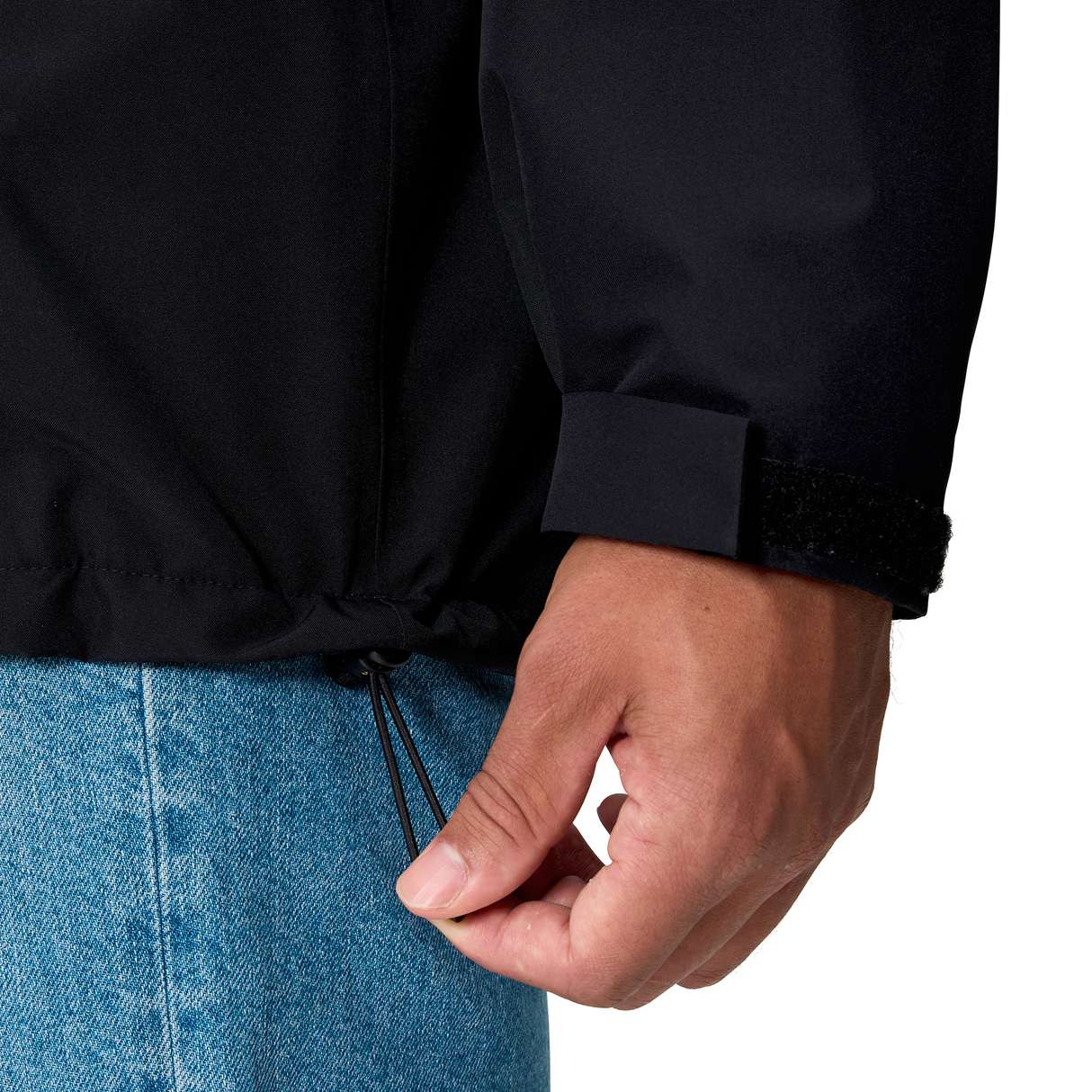 A person in blue jeans uses one hand to tighten the hem drawstring of a Canterbury Ireland 25/26 Water Resistant Insulated Jacket.