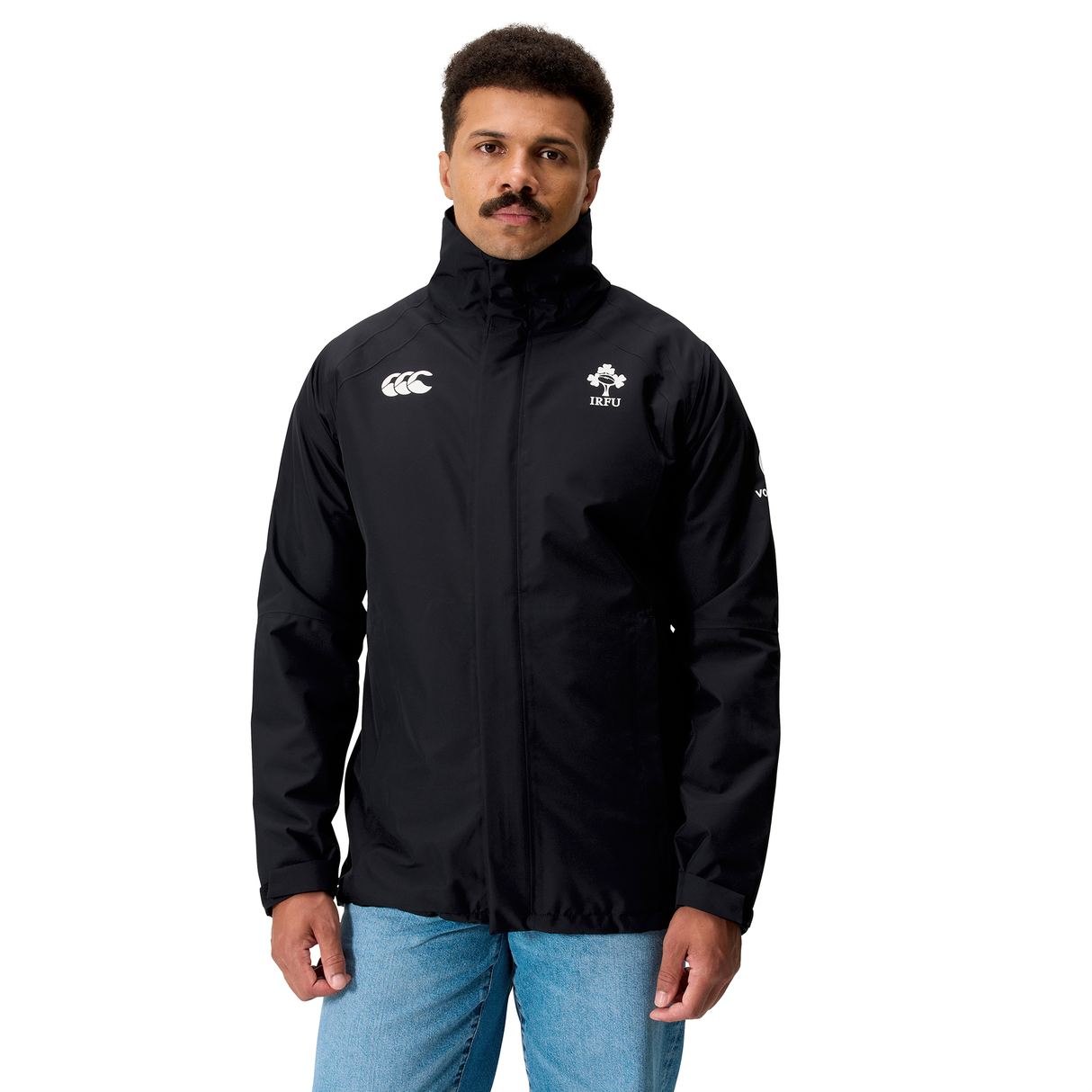 A man wearing the Canterbury Ireland 25/26 Water Resistant Insulated Jacket, featuring white logos on the chest, paired with blue jeans and standing against a white background.