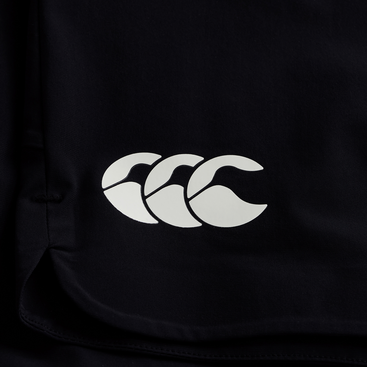 Close-up of black fabric with a white Canterbury logo—three overlapping C’s—featured on the official Ireland 25/26 Gym Training Short by Canterbury.