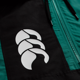 A close-up of the Ireland 25/26 Legends 1/4 Zip Jacket by Canterbury features a white abstract logo and visible green zipper, emphasizing the brand's stylish quarter-zip design.
