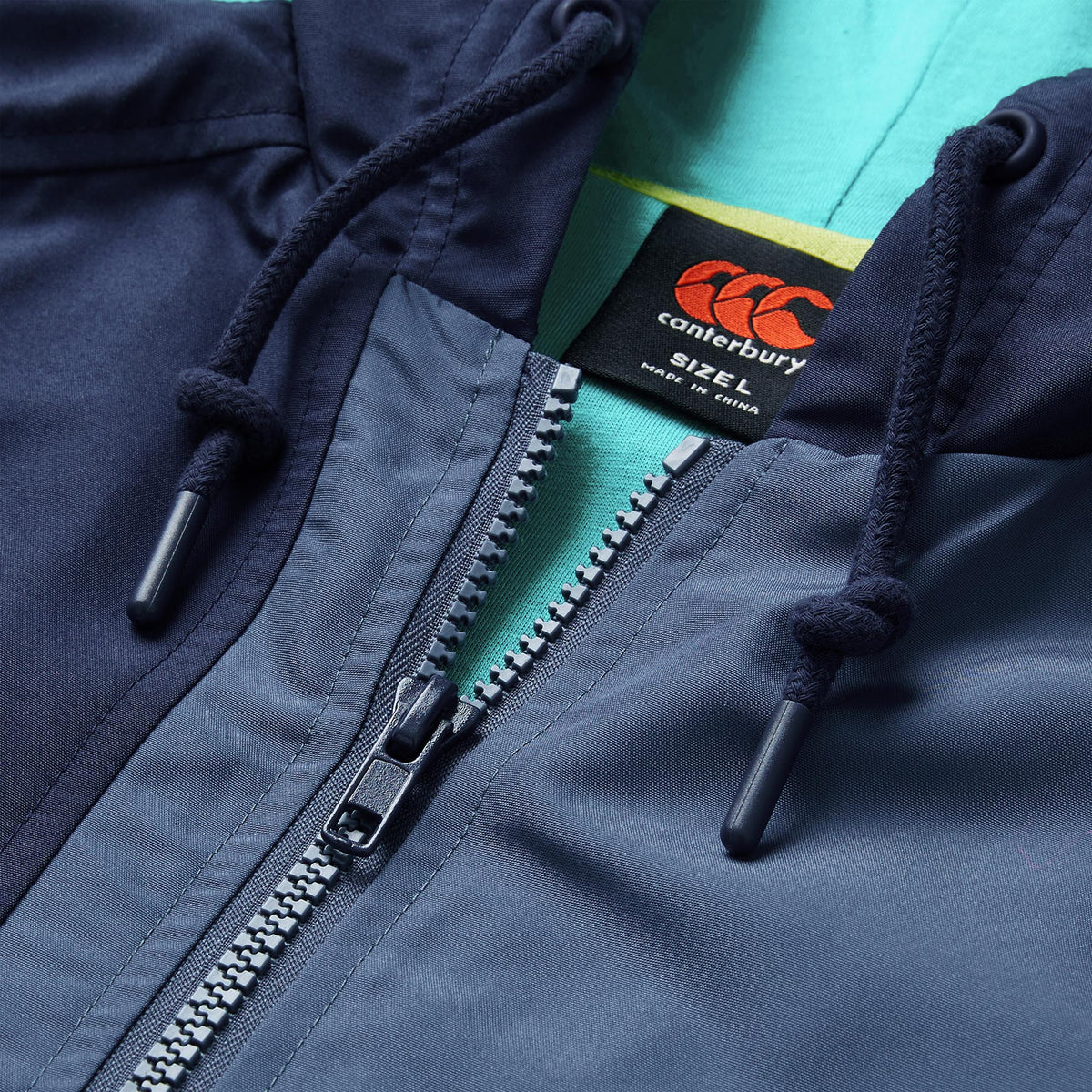 Close-up of the Ireland 26 Legends 1/4 Zip Jacket by Canterbury in navy blue, featuring a hood with drawstrings and Canterbury branding, layered over a green shirt—a modern tribute to the classic Ireland Rugby style.