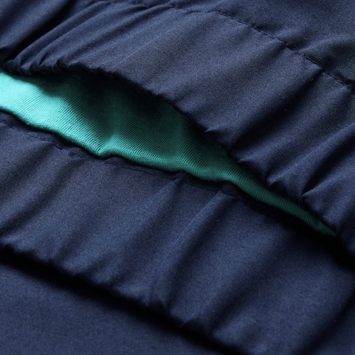 Close-up of gathered navy blue fabric from the Canterbury Ireland 26 Legends 1/4 Zip Jacket, with a visible layer of light teal fabric underneath.