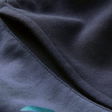 Close-up of a dark blue fabric with visible stitching and a fold, highlighting the texture and part of a teal design in the lower left corner—capturing the premium detail characteristic of the Ireland 26 Legends 7″ Shorts by Canterbury.