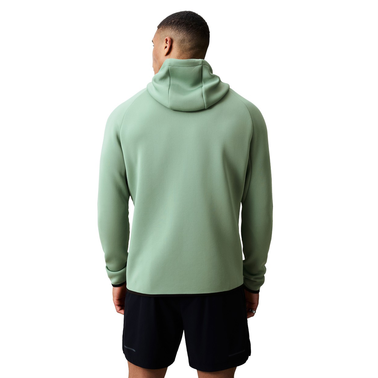 A person wearing a light green Canterbury Everest Zip Thru Hoodie by Canterbury and black shorts stands with their back to the camera against a white background.