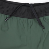 Close-up of the waistband of green Canterbury Everest Woven Short 5" athletic shorts, featuring a black elastic band and center-tied drawstring. Made from four-way stretch fabric for comfort during training. Brand: Canterbury.