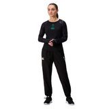 A woman stands against a white background wearing a black long-sleeve shirt, black sneakers, and Canterbury Women's Ireland 25/26 Training Pants featuring branded logos.