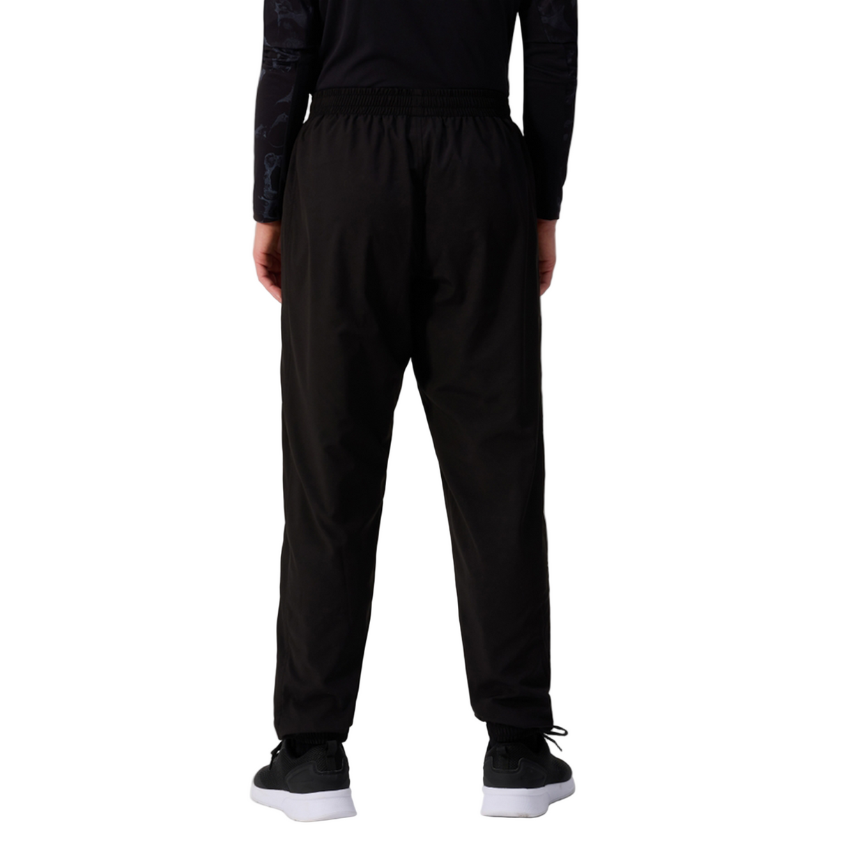 A person faces away, wearing Canterbury Women's Ireland 25/26 Training Pant with an athletic tapered fit, a long-sleeve black top, and black sneakers with white soles against a white background.
