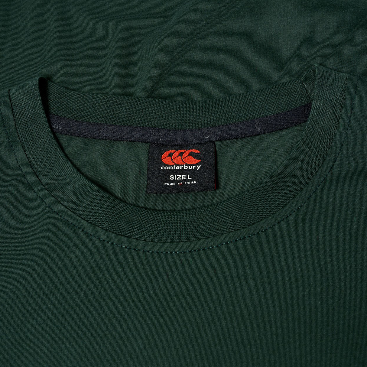 Close-up of a dark green Canterbury FUN. T-SHIRT AM, focusing on the collar and inside label showing size L and made in China.