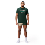 A man faces forward against a white background, wearing a dark green Canterbury FUN. T-SHIRT AM with logo, beige athletic shorts, white socks, and white shoes.