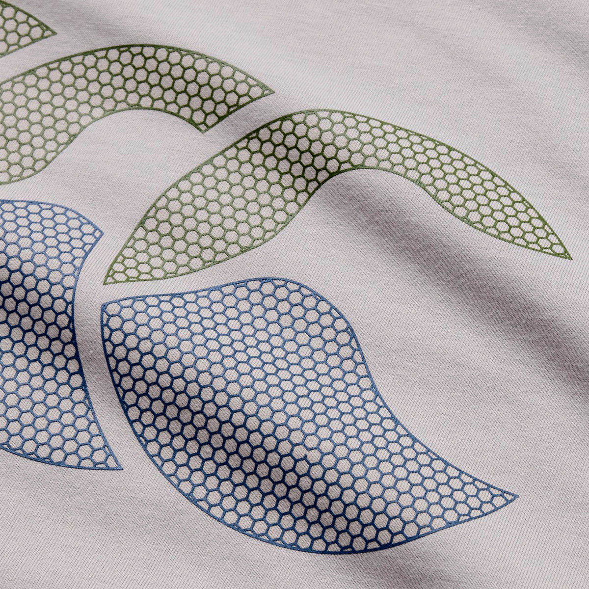 Showcasing an abstract design on fabric, the Canterbury Fundamentals T-shirt by Canterbury features two green and two blue curved shapes over a hexagonal mesh pattern, circularly arranged on a light background—making it ideal for athletic casual wear or as a bold accent on a rugby t-shirt.