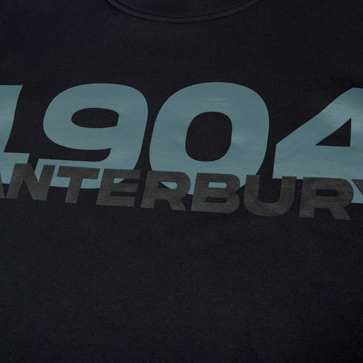 Close-up of Canterbury's EVERYDAY GFX CREW SWEATER in black, featuring bold blue "1904" numbers and partially visible "CANTERBURY" text—ideal for everyday wear.
