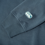 A close-up of the Canterbury EVERYDAY GFX CREW SWEATER’s blue cuff and sleeve, showing a small embroidered logo with two white shapes in an oval—ideal for stylish everyday wear.