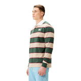 A man stands against a white background wearing the Canterbury Stripe Rugby Jersey by Canterbury, featuring green, beige, and red stripes with a white collar, paired with light blue jeans.