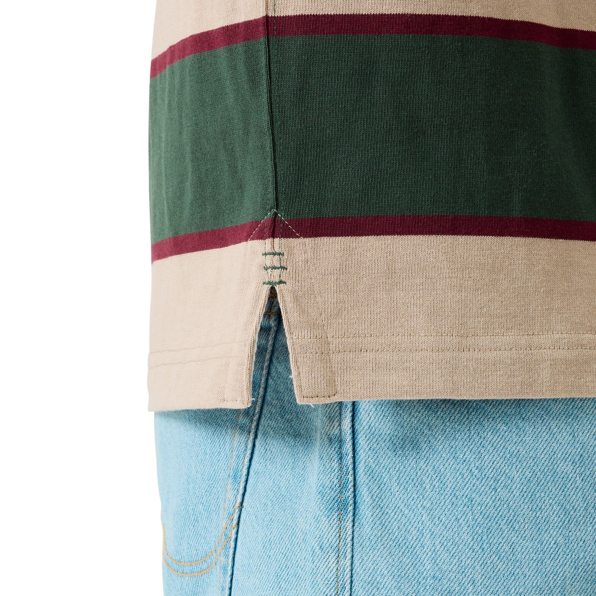 Close-up of the Canterbury Stripe Rugby Jersey by Canterbury in beige, green, and maroon with a side slit hem, styled over light blue denim jeans.