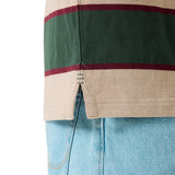 Close-up of the Canterbury Stripe Rugby Jersey by Canterbury in beige, green, and maroon with a side slit hem, styled over light blue denim jeans.