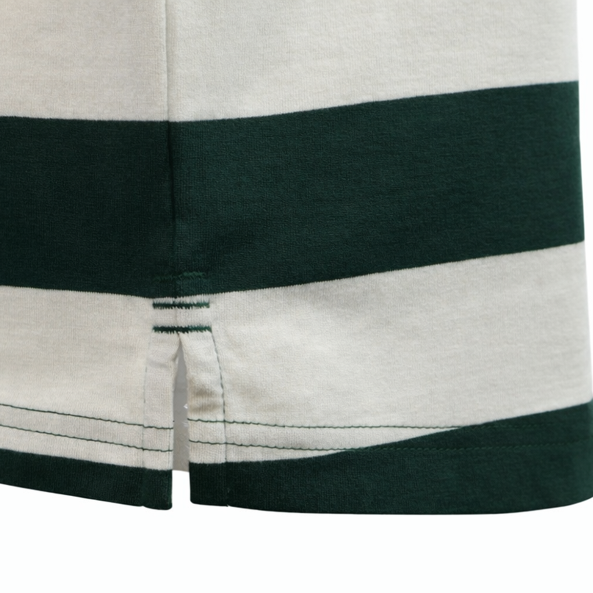 Close-up of the hem on the Canterbury Yarn Stripe Polo by Canterbury in white and dark green, showing a small side slit and visible stitching that emphasize its classic rugby style.