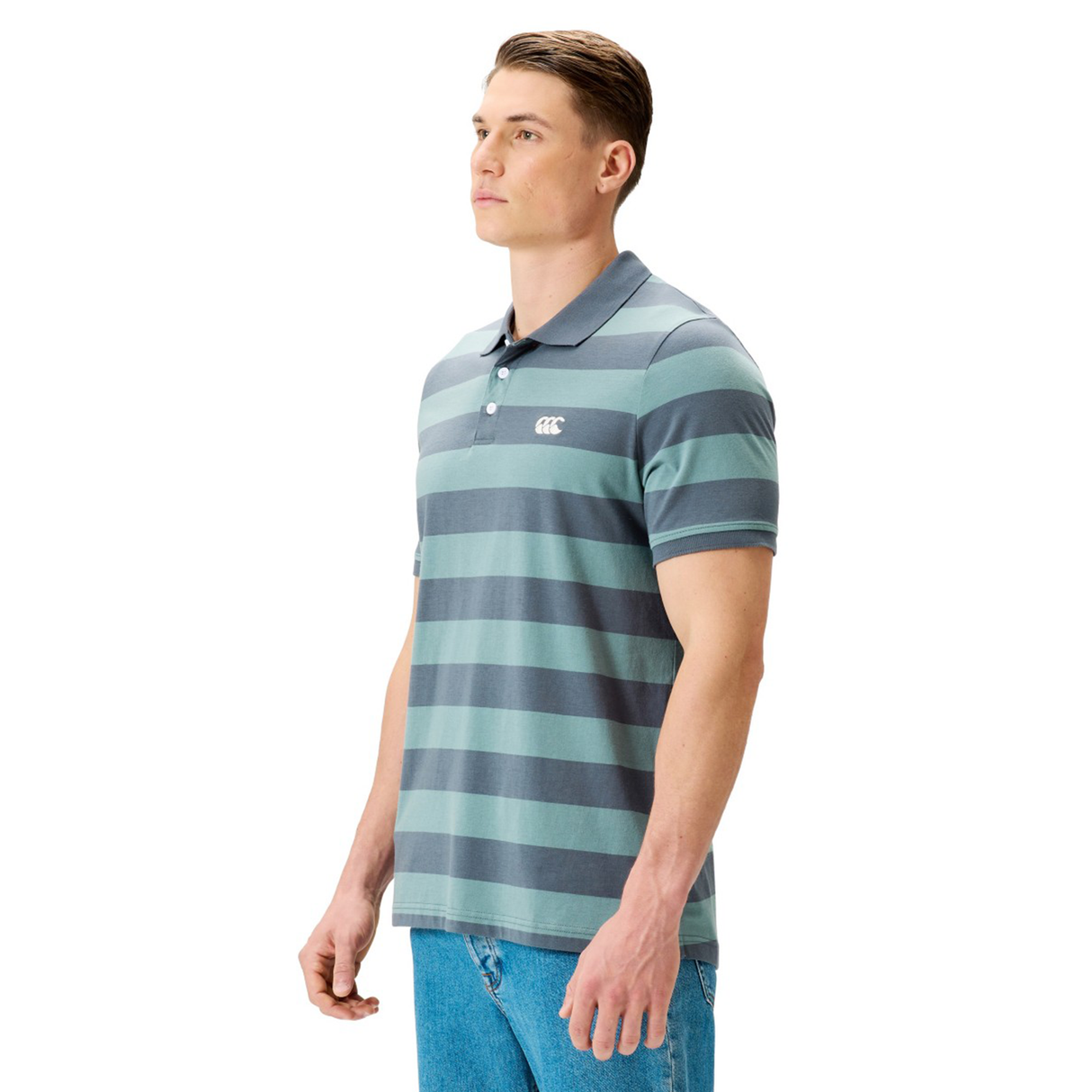A man stands against a plain white background wearing the Canterbury Yarn Stripe Polo by Canterbury, featuring blue and gray stripes, classic rugby styling, and a chest logo.