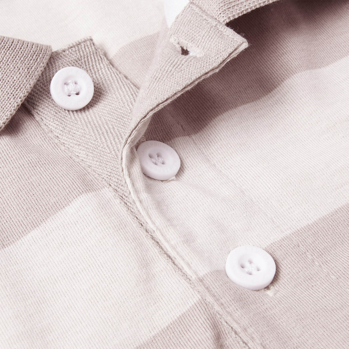 Close-up of the Canterbury Yarn Stripe Polo by Canterbury, showcasing its beige and white stripes, white buttons, and classic collar—highlighting the textured fabric and button placket that embody the timeless appeal of a rugby-inspired style.