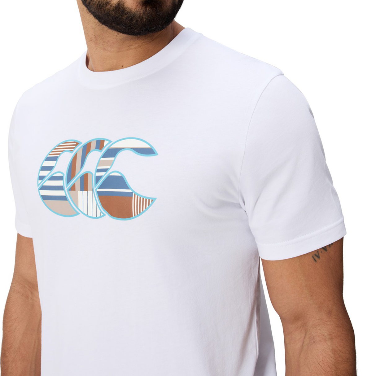 Man in a Canterbury Uglies Logo T-shirt by Canterbury, featuring a multicolored chest graphic and made from a white cotton blend, shows off a small upper arm tattoo.