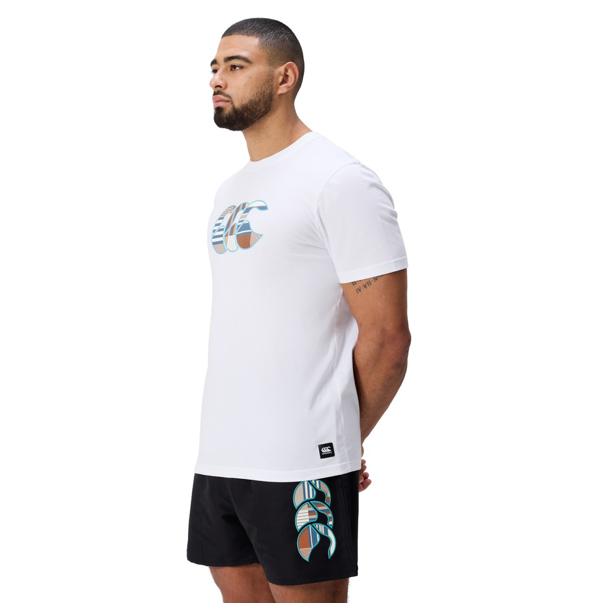 A man faces left, wearing a white Canterbury Uglies Logo T-shirt in a soft cotton blend and black shorts with matching graphics, set against a plain white background.