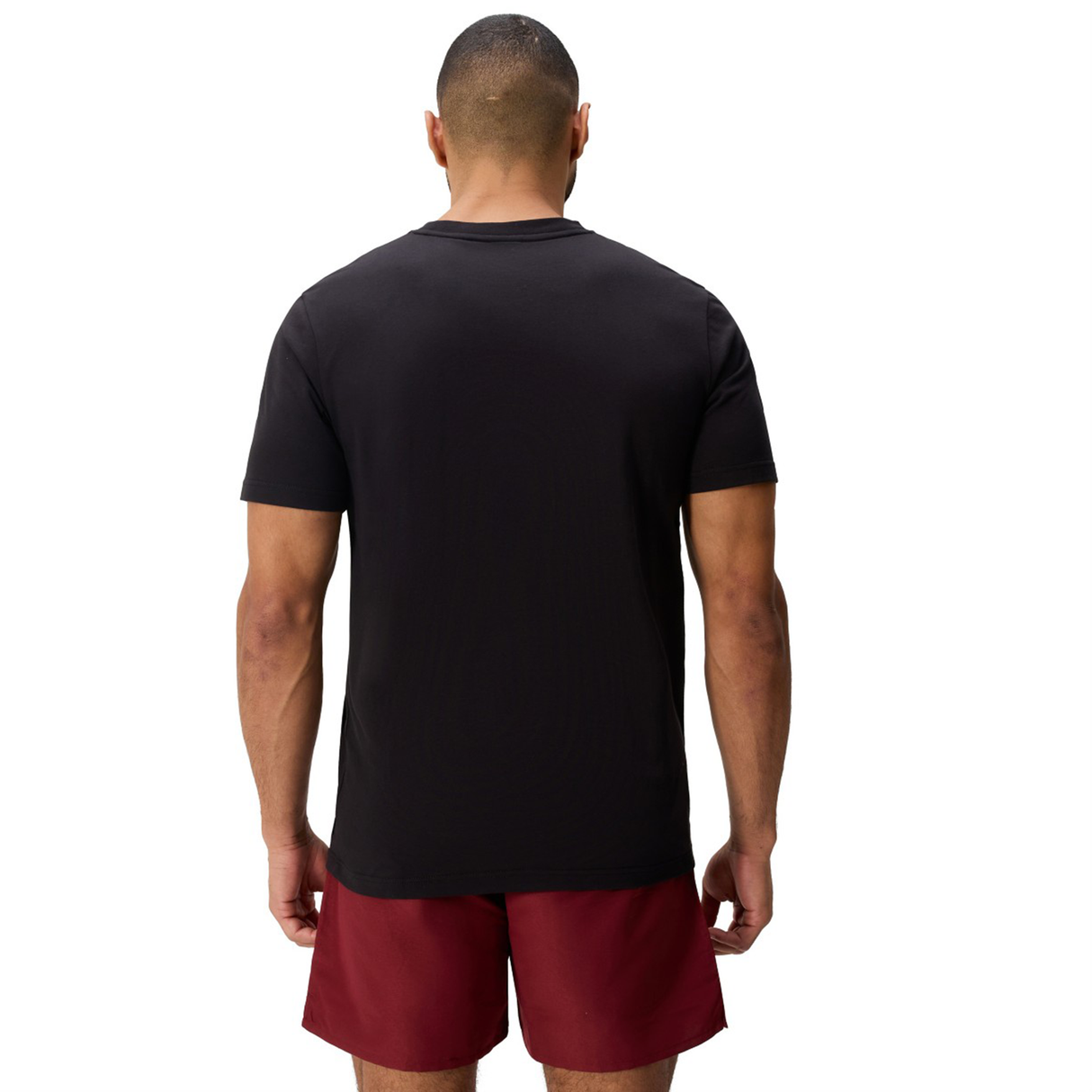 A person stands facing away from the camera, wearing a Canterbury Uglies Logo T-shirt by Canterbury and maroon shorts against a white background.