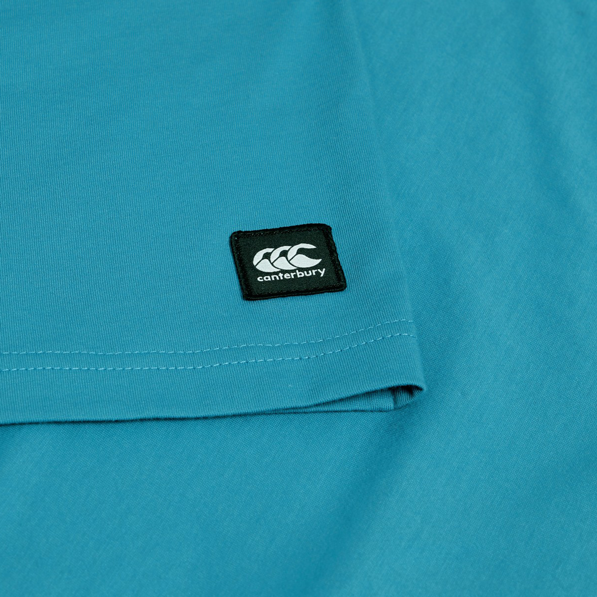 Close-up of the Canterbury Uglies Logo T-shirt, a teal cotton blend tee with a small black rectangular Canterbury patch displaying the white logo and text.