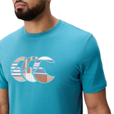 A man wears a Canterbury Uglies Logo T-shirt by Canterbury, featuring a turquoise cotton blend and striped graphic logo on the chest, shown from the shoulders up against a white background.