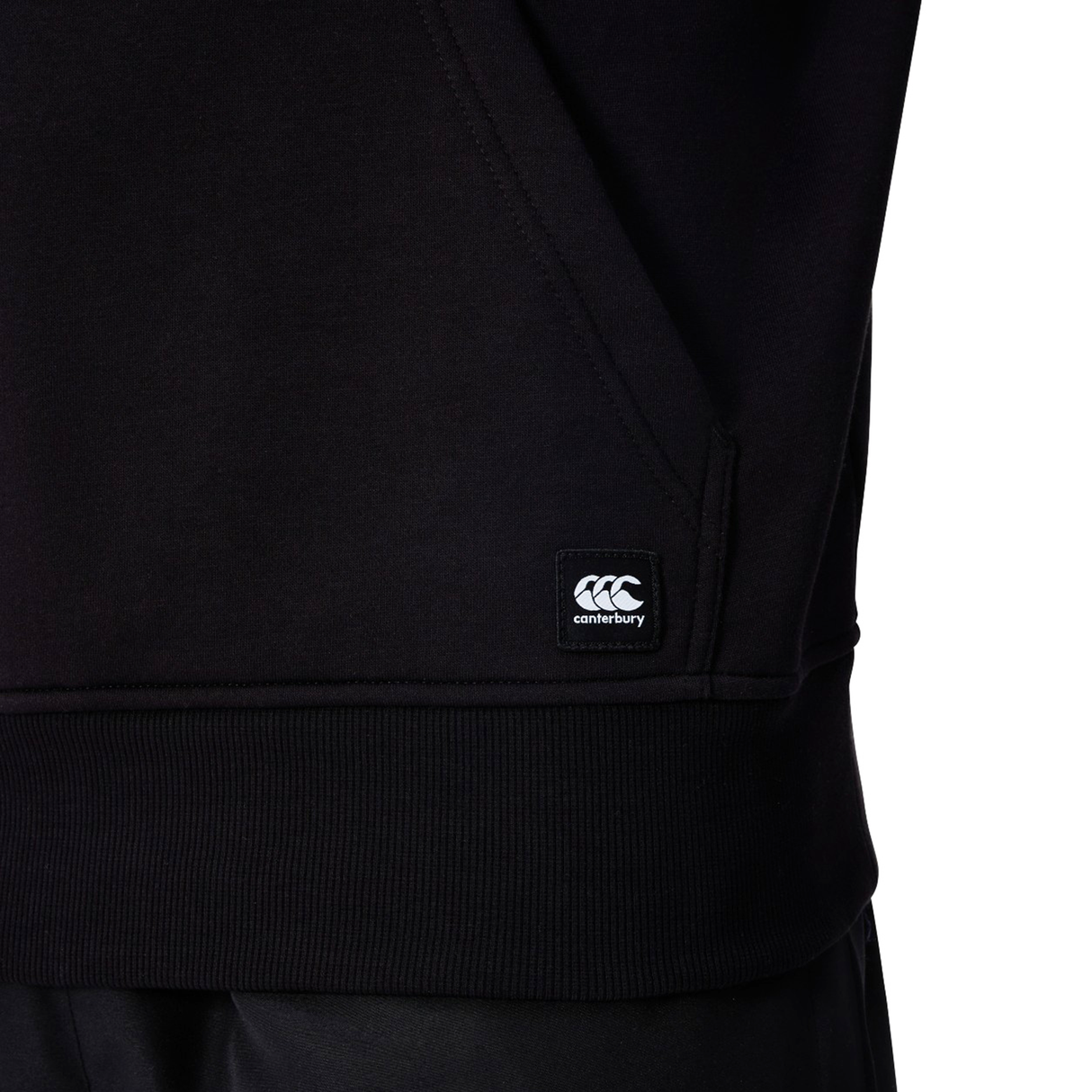 Close-up of the Canterbury Uglies Logo Hoodie by Canterbury, featuring a logo tag near the pocket, ribbed hem, and detailed pocket seam—ideal for rugby hoodie fans.