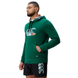 A man wearing a green Canterbury Uglies Logo Hoodie with a colorful design and black shorts with a matching pattern stands facing left against a white background.