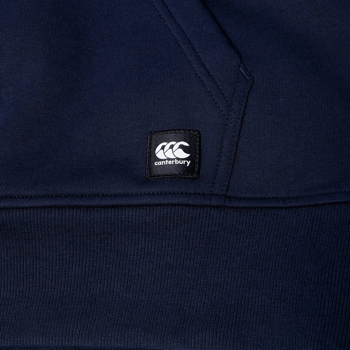 Close-up of a navy blue Canterbury Uglies Logo Hoodie, showcasing a visible pocket seam and a black Canterbury logo patch.