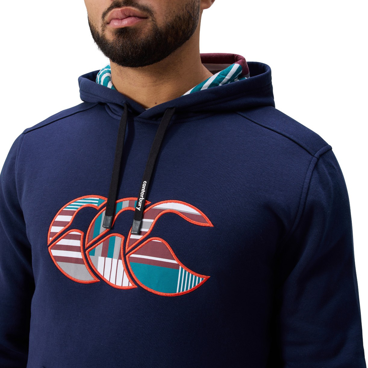 A man wears the Canterbury Uglies Logo Hoodie in navy blue, featuring a colorful abstract logo on the chest and black drawstrings by Canterbury, set against a plain white background.