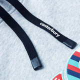 Close-up of the Canterbury Uglies Logo Hoodie drawstrings, featuring "canterbury" text on one lace, resting on light gray fabric with a glimpse of the colorful embroidered logo—a signature detail reflecting Canterbury’s bold rugby style.