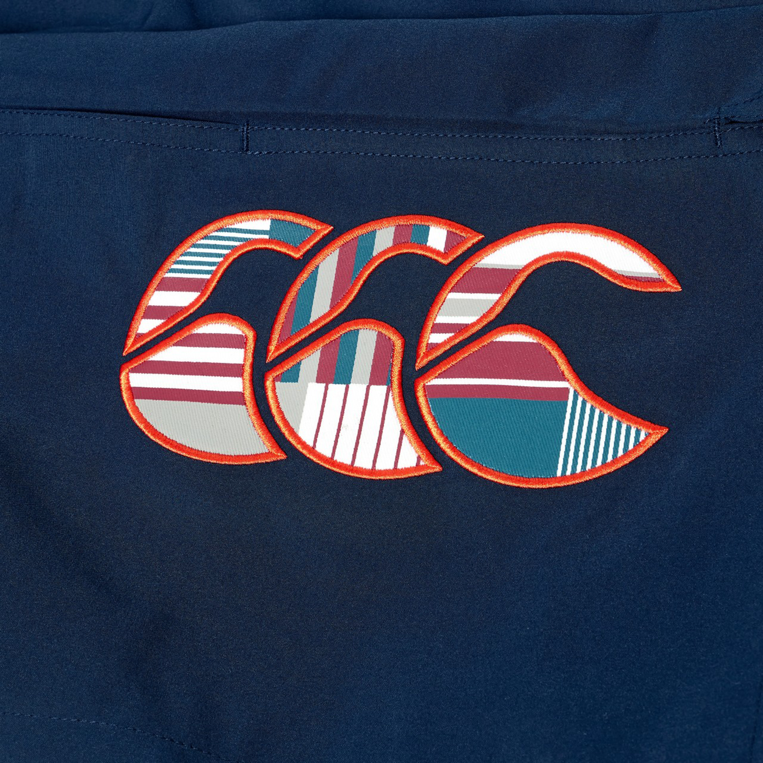 Close-up of the colorful "CCC" logo from Canterbury's Uglies 5" Tactic Short, showcasing a vibrant patterned design on dark blue fabric—ideal for durable rugby or training shorts.