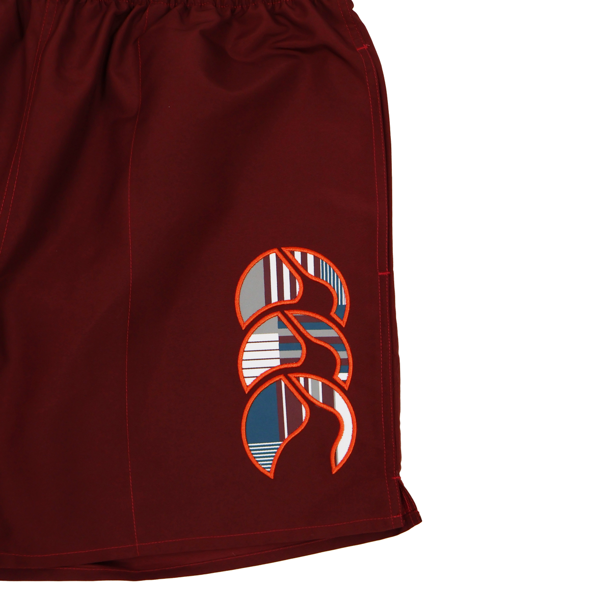 A close-up of Canterbury Uglies 5" Tactic Shorts in maroon, featuring an abstract geometric logo in white, orange, navy, and gray on the left leg—durable training shorts ideal for any athlete.