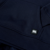 Close-up of the Canterbury Youth Uglies Logo Hoodie in navy blue, featuring a prominent Canterbury logo patch near the pocket and ribbed cuff detail, highlighting classic rugby style inspired by the iconic Canterbury Uglies collection.