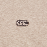 A close-up of beige fabric from the Canterbury FORCE HOODIE, showing a small embroidered logo with three overlapping black waves inside an oval outline.
