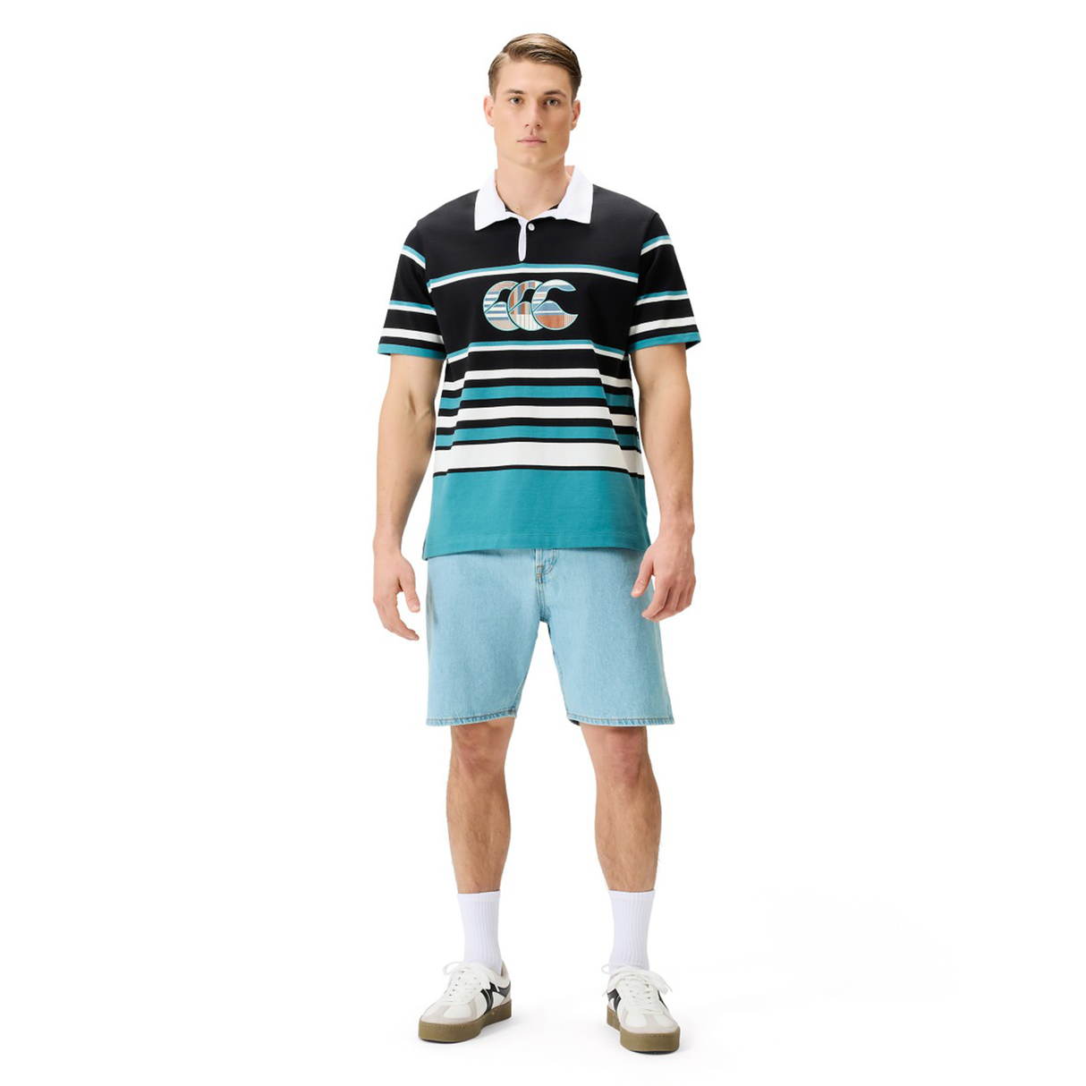 A man faces forward, wearing a Canterbury Uglies Short Sleeve Classic Rugby Jersey by Canterbury, paired with light blue denim shorts, white socks, and sneakers, set against a plain white background.