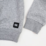 Close-up of a gray Canterbury Women's Uglies Logo Crew Sweatshirt displaying ribbed cuffs and a black Canterbury CCC logo patch near the hem on a white background.