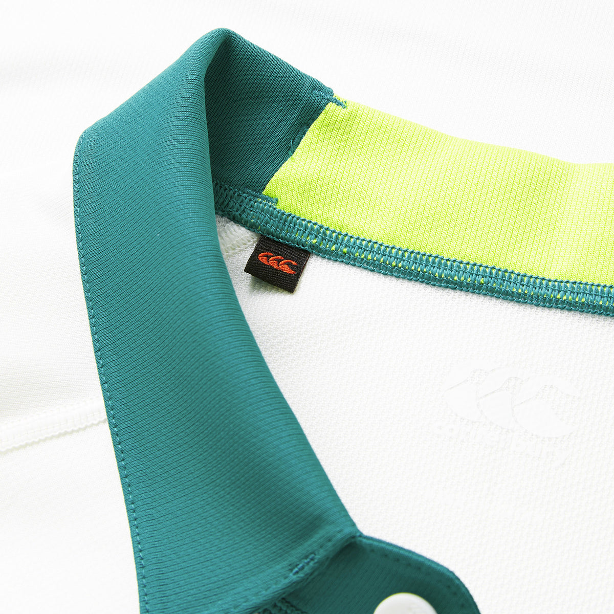 Close-up of the Ireland 26 Alternate Pro Jersey by Canterbury—a white rugby jersey featuring a teal collar, lime green inner collar detail, white buttons, and a black clothing tag with Canterbury’s red logo—showcasing the crisp styling characteristic of classic Canterbury jerseys.