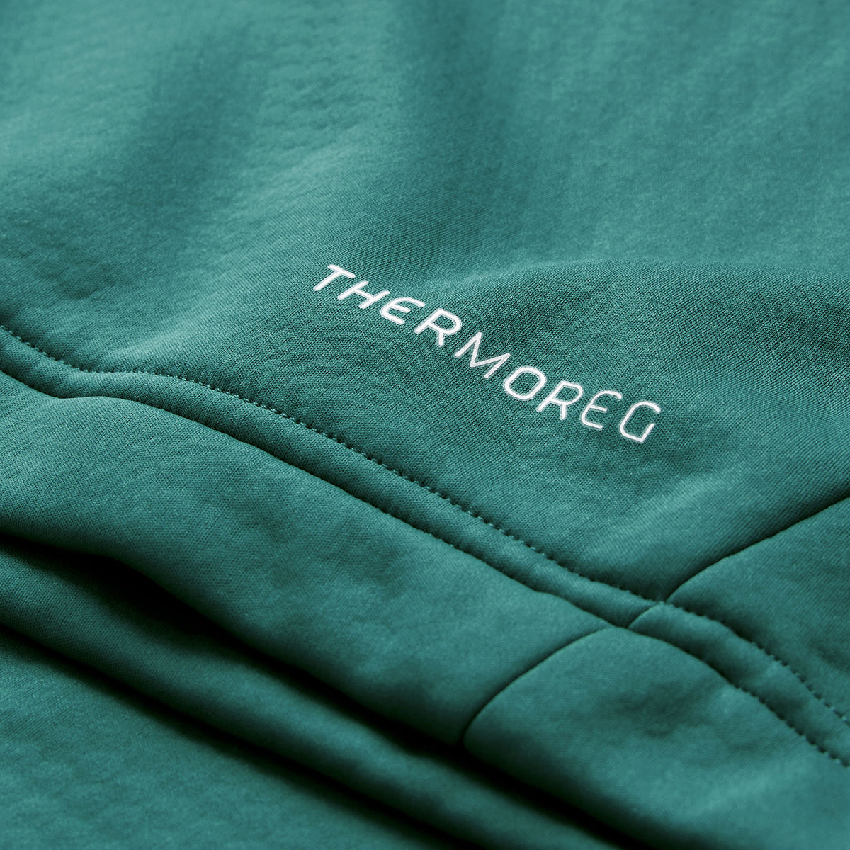 Close-up of green fabric from the Ireland 26 1/4 Zip Training Top by Canterbury, featuring the word “THERMOREG” stitched in white thread, highlighting the advanced Thermoreg technology incorporated in this Canterbury top.