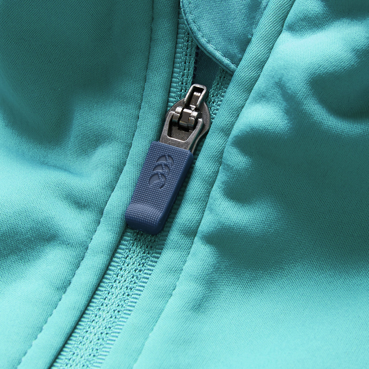 Close-up of the Ireland 26 1/4 Zip Training Top by Canterbury in teal fabric, inspired by Ireland rugby, featuring a prominent blue zipper and pull tab in a partially zipped position.