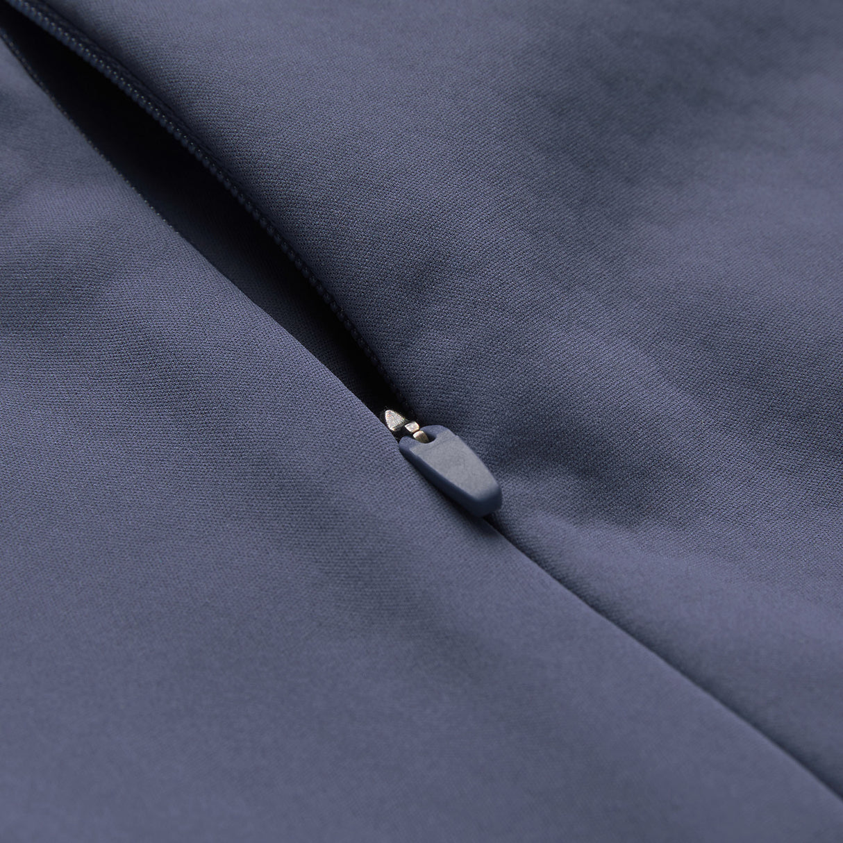 Close-up of the Canterbury Ireland 26 1/4 Zip Training Top in gray, partially zipped on a smooth fabric surface, highlighting the zipper pull and stitching details. This training top is equipped with Canterbury’s advanced Thermoreg technology for superior comfort.