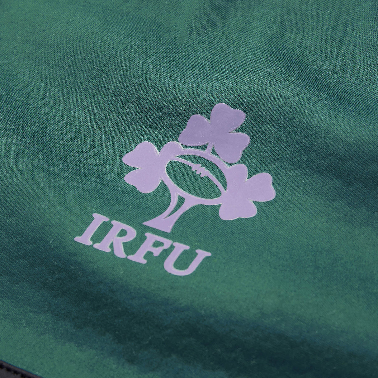 Close-up of the IRFU (Irish Rugby Football Union) logo with three shamrocks and a rugby ball on green fabric, highlighting the Ireland 26 1/4 Zip Training Top by Canterbury, crafted with advanced Thermoreg technology.