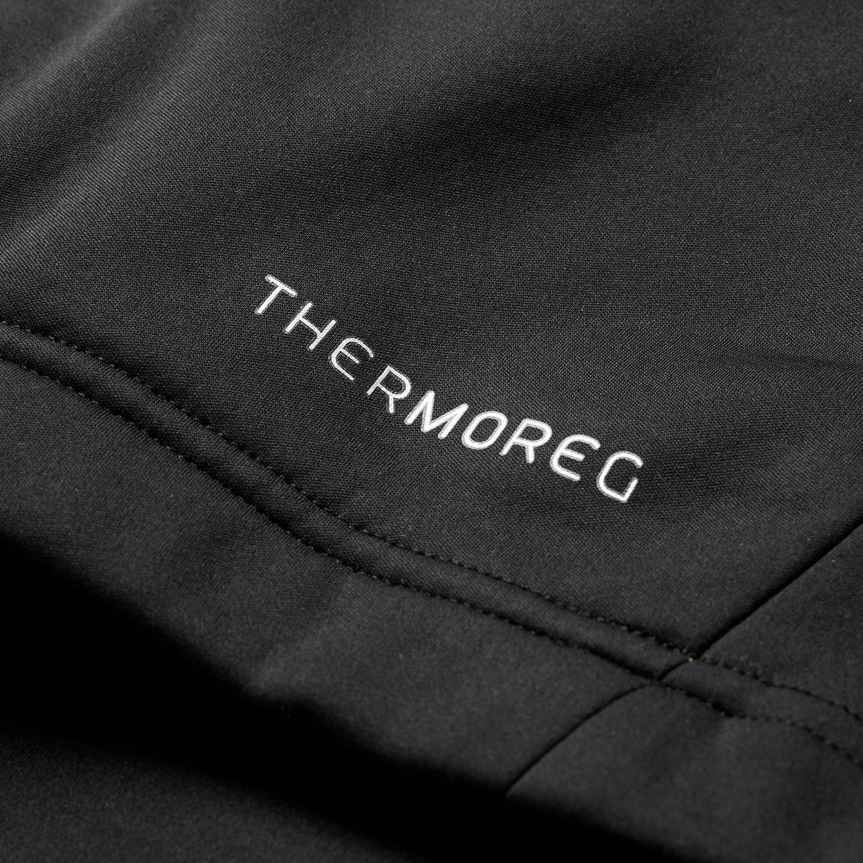 Close-up of black fabric with white embroidered “THERMOREG” text and visible seam detailing, highlighting the advanced Thermoreg technology featured in the Ireland 26 1/4 Zip Training Top by Canterbury.