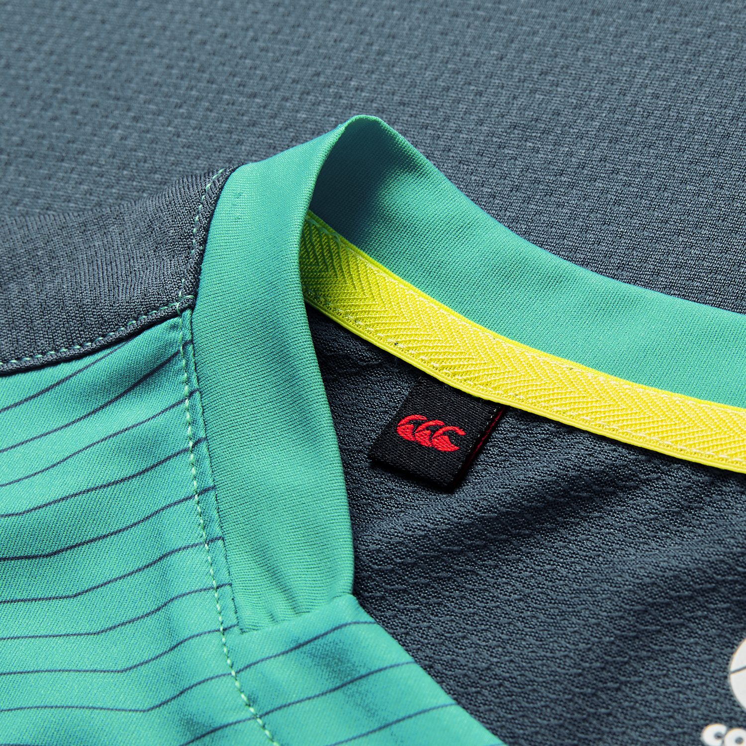 Close-up of the Ireland 26/27 Summer Tour Superlight Training Tank by Canterbury, featuring a teal collar with yellow inner trim, black tag with red logo, and detailed stitching—ideal for fans of lightweight training wear.
