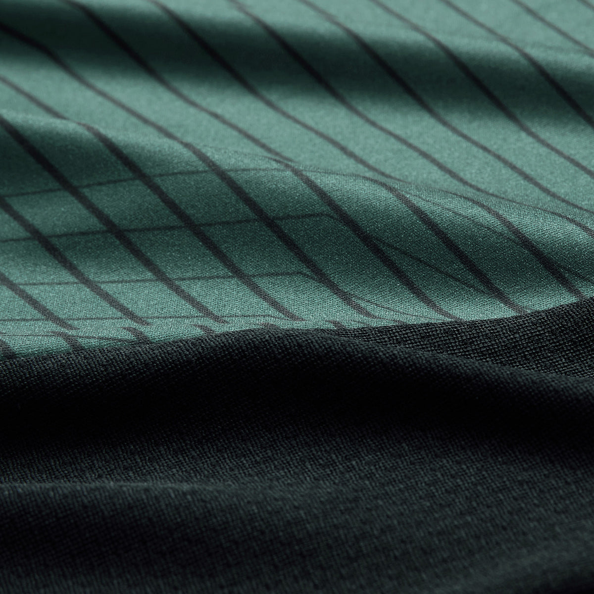 Close-up of green fabric with thin vertical black stripes above a section of solid black fabric, highlighting the texture and folds—typical detailing found on the Ireland 26 Training Tank by Canterbury AW26, designed for performance and comfort by Canterbury.