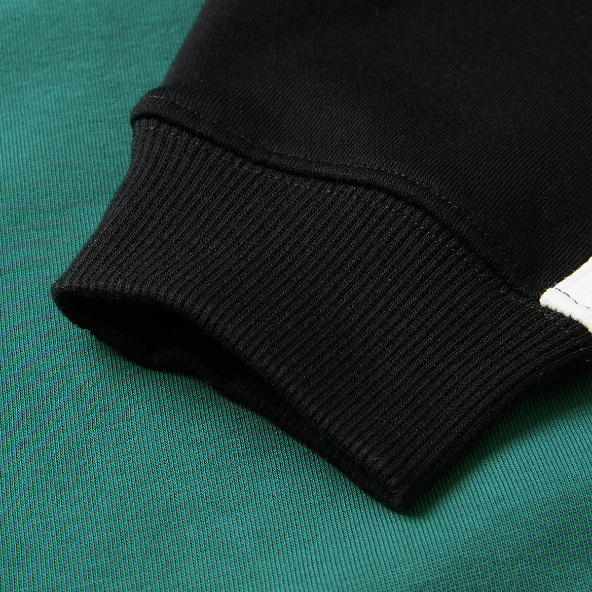 Close-up of the sleeve of the Women’s Ireland 26 Legends 1/4 Zip Sweatshirt by Canterbury resting on a green fabric surface, highlighting the texture and stitching details of the materials.