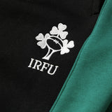 Close-up of a black and green fabric from the Canterbury Women’s Ireland 26 Legends Fleece Pant, featuring an embroidered white IRFU logo with three shamrocks and a rugby ball.