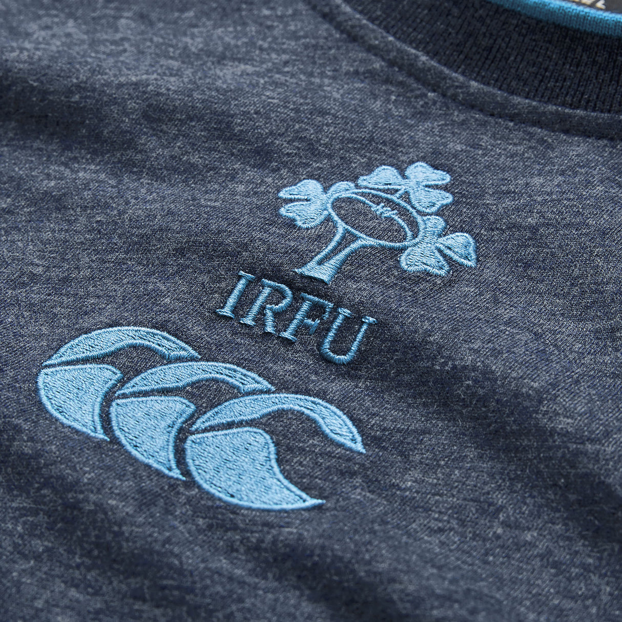 Close-up of a dark grey Women’s Ireland 26 Cotton T-shirt by Canterbury, showcasing the light blue embroidered IRFU logo with shamrock symbol and the distinctive Canterbury brand logo.